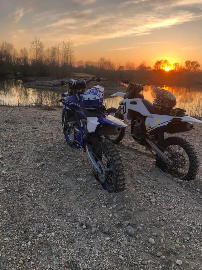 Two motocross bikes parked by a river at sunset.