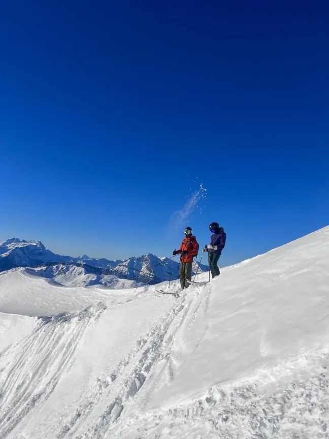 Two skiers standing at the top of a ridge under a deep blue sky.